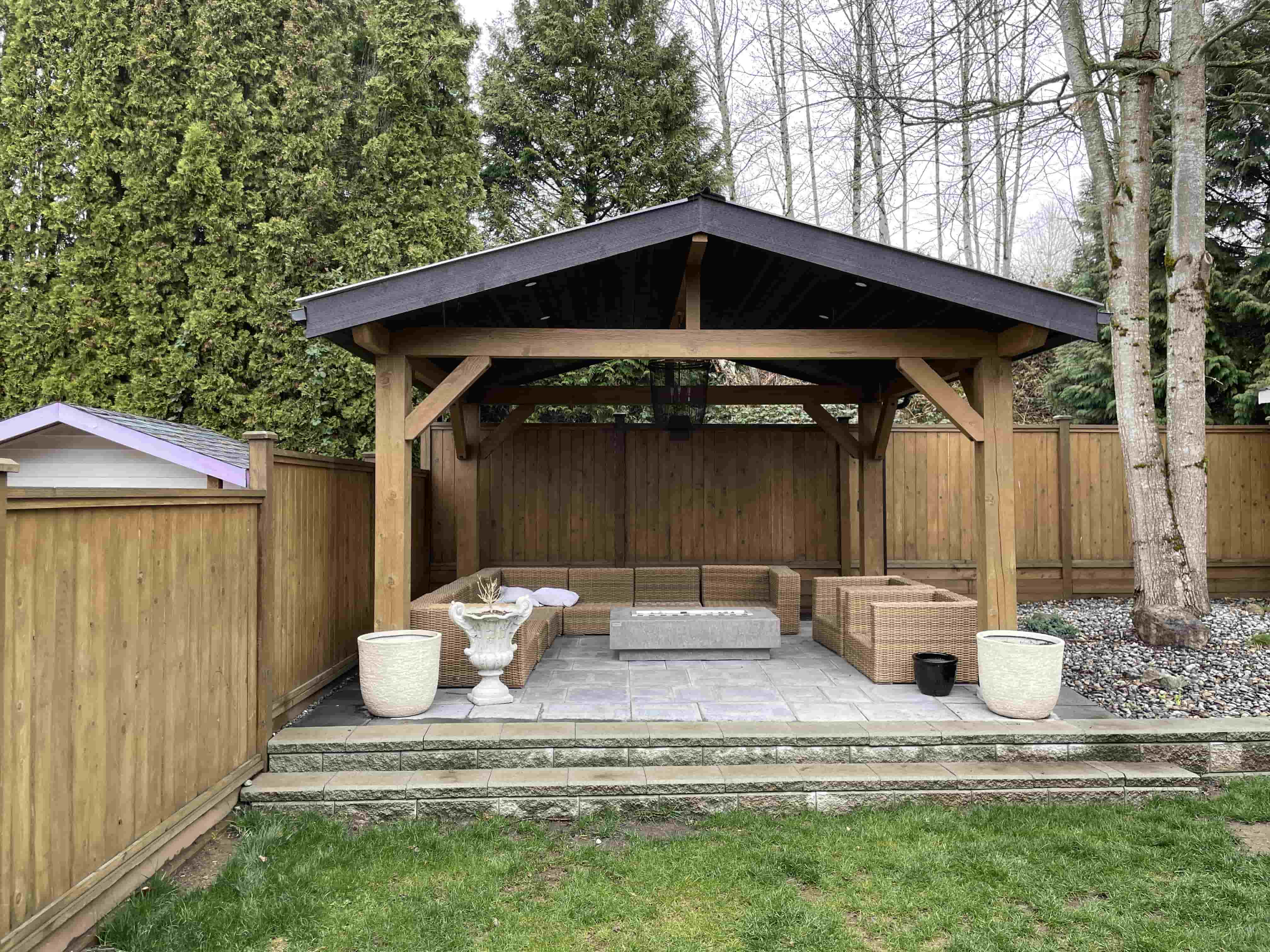 a post and beam gazebo constructed in a backyard covering outdoor seating & a fire pit