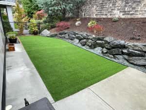 backyard artificial turf installation with a natural rock retaining wall